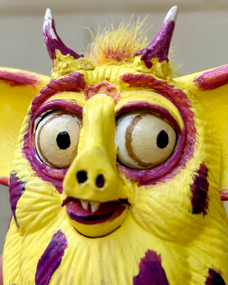 a close up of the Furby’s face. he is looking to the side and has tiny fangs and a pig like nose 
