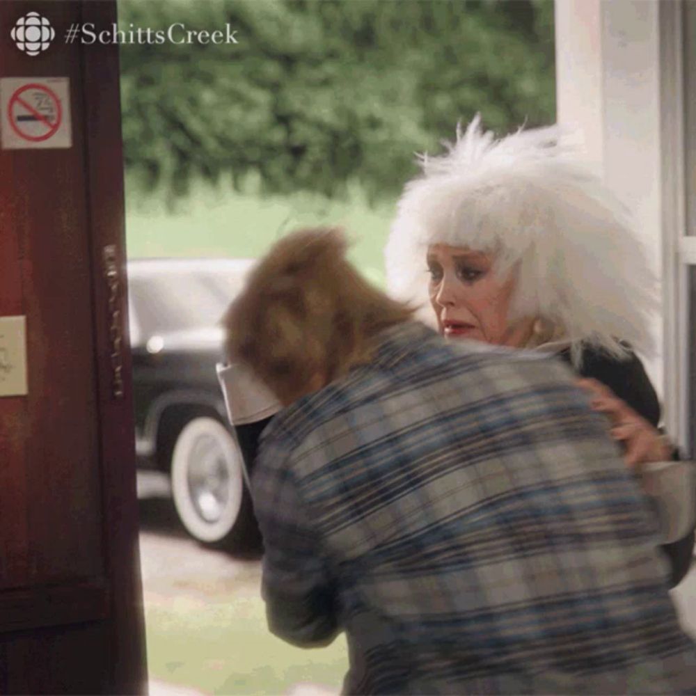 a woman in a white wig is hugging a man in front of a sign that says no smoking