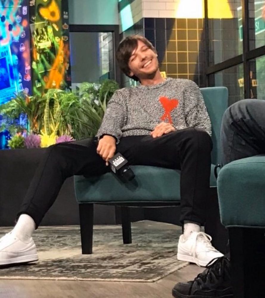 Louis Tomlinson sits for Walls album promo in a grey sweatshirt and red Ami heart 