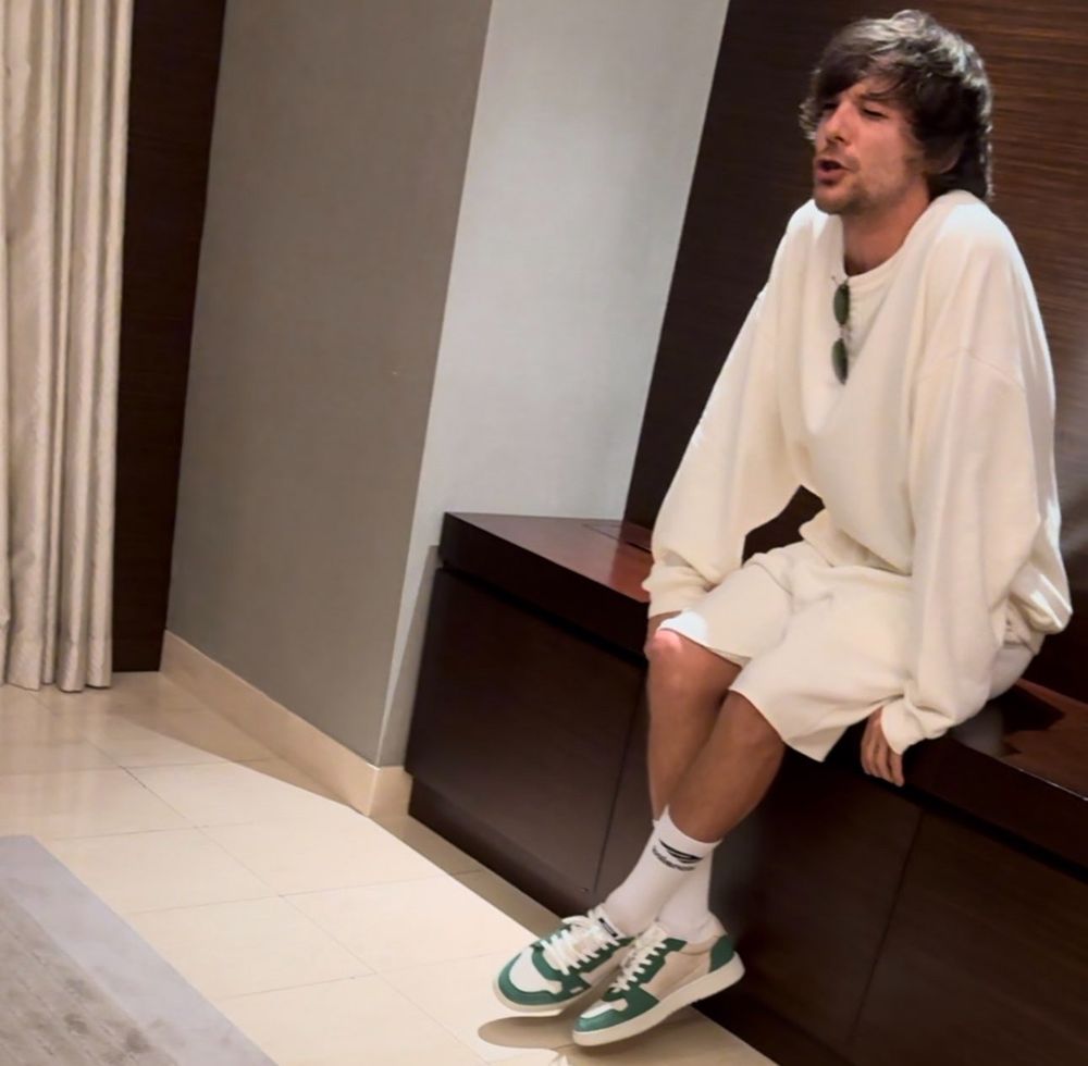 Louis stuns in all white, a cozy oversized white sweatshirt and white shorts, with green shoes and sunglasses. His hair is long and puffy, and he’s got sweaterpaws in the sweatshirt