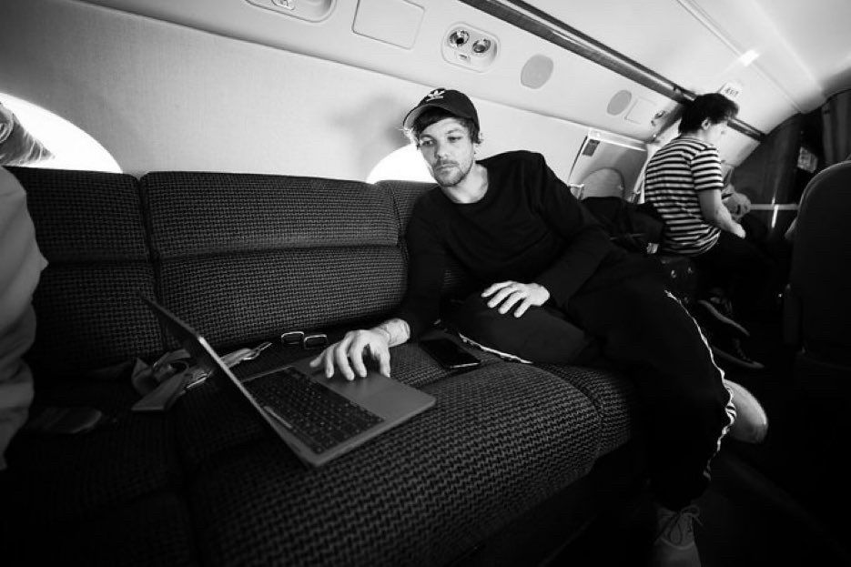 CEO on a plane a Louis sits with his laptop, leaned over touching the trackpad.