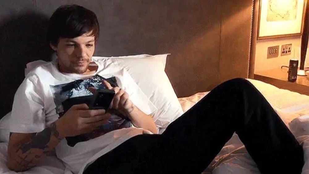 Louis sits on his bed scrolling on his phone