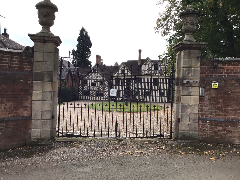 Colour image of a medieval timber framed hall includes the modern gates.