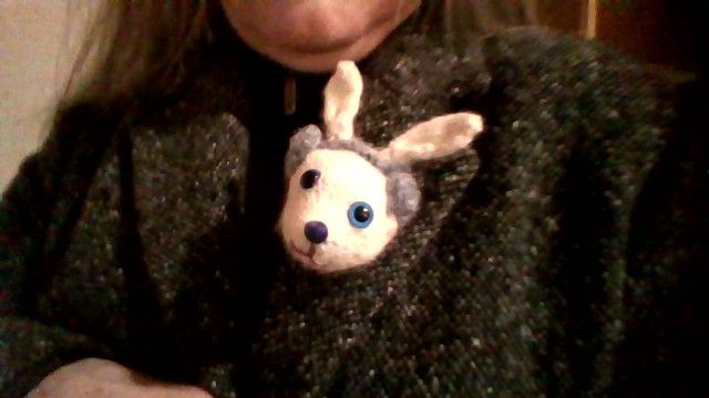 Hand knitted white mouse head brooch on the lapel of a black and white Donegal tweed coat. The mouse has little grey earmuffs/headphones on.