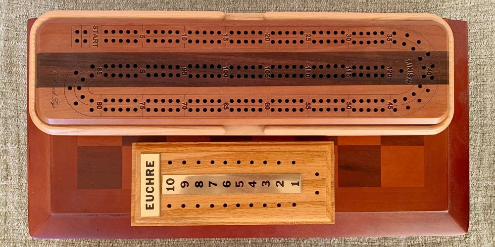 Two-toned wooden game boards for chess and cribbage, and a score-keeping board board for euchre, with metal plates for numbers (1 to 10) and the game name