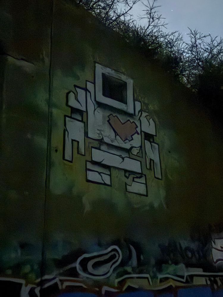 A fuckin sick square robot graffitied onto a concrete underpass. It has a big heart and loves you, probably.