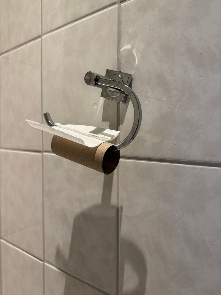 Aufgebrauchte Klopapierrolle am Halter, das letzte Blatt oben aufliegend.