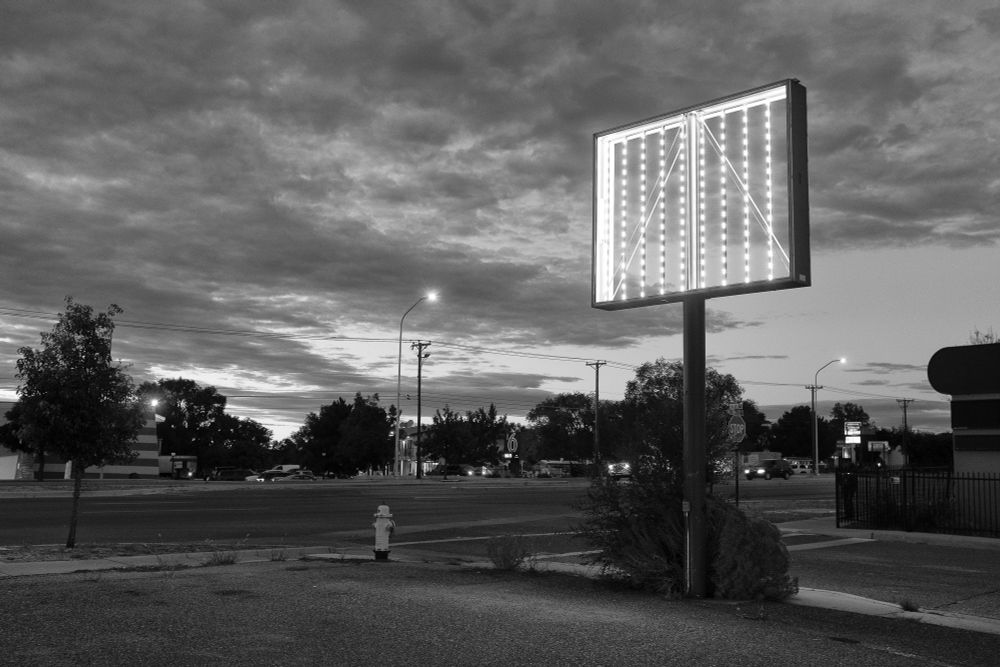 Twilight sky with clouds. Illuminated sign frame missing the sign on the corner of a commercial parking lot. A beacon.