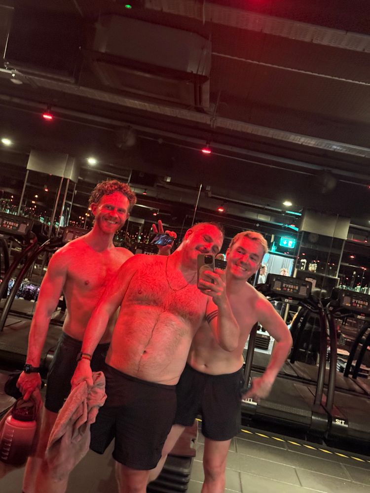 Three shirtless men in a gym under red lights 
