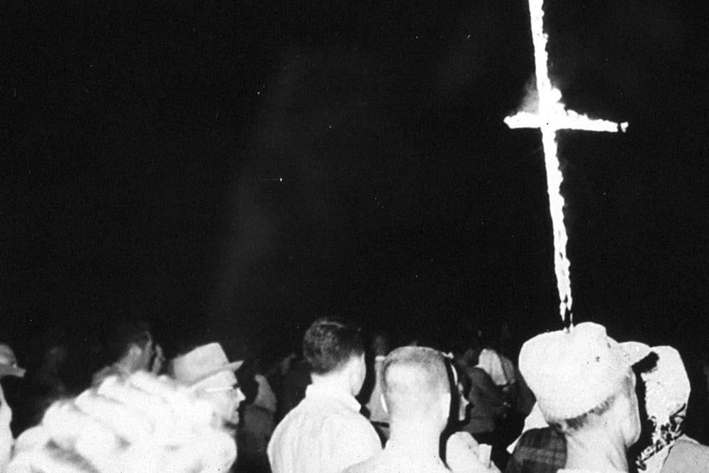 Black and white photo of a cross burning at a KKK rally