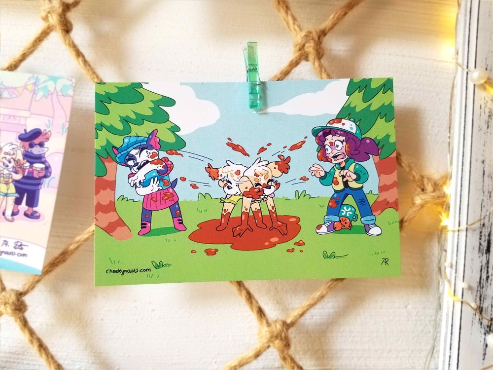 Photo of physical postcard featuring following illustration: Martha the puppy shakes mud off herself onto Dot the dog pack boss and the Moonshell Island protagonist in a forest setting in comedic fashion