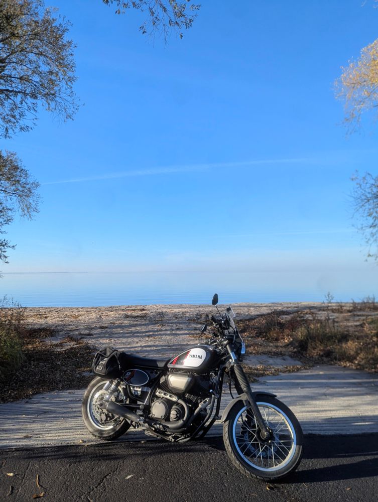 a bike parked in front of a sandy walkway spilling out into a glassy, cotton candy-colored body of water