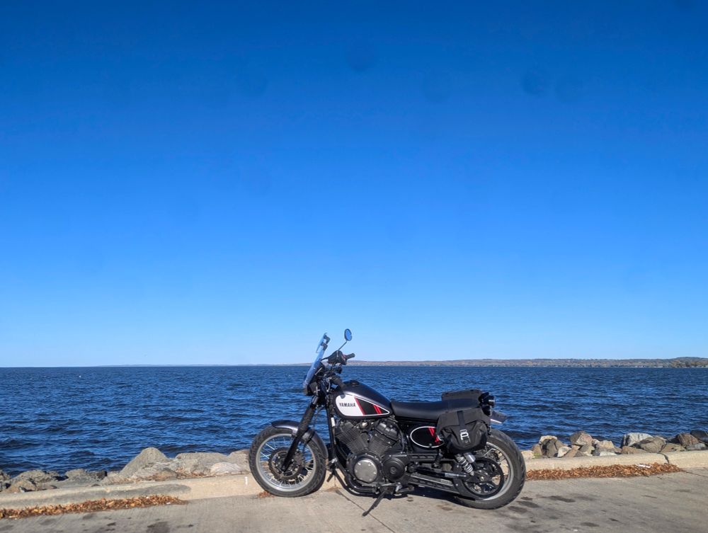 motorcycle parked by the shore, overlooking a large body of water under a brilliant, blue sky