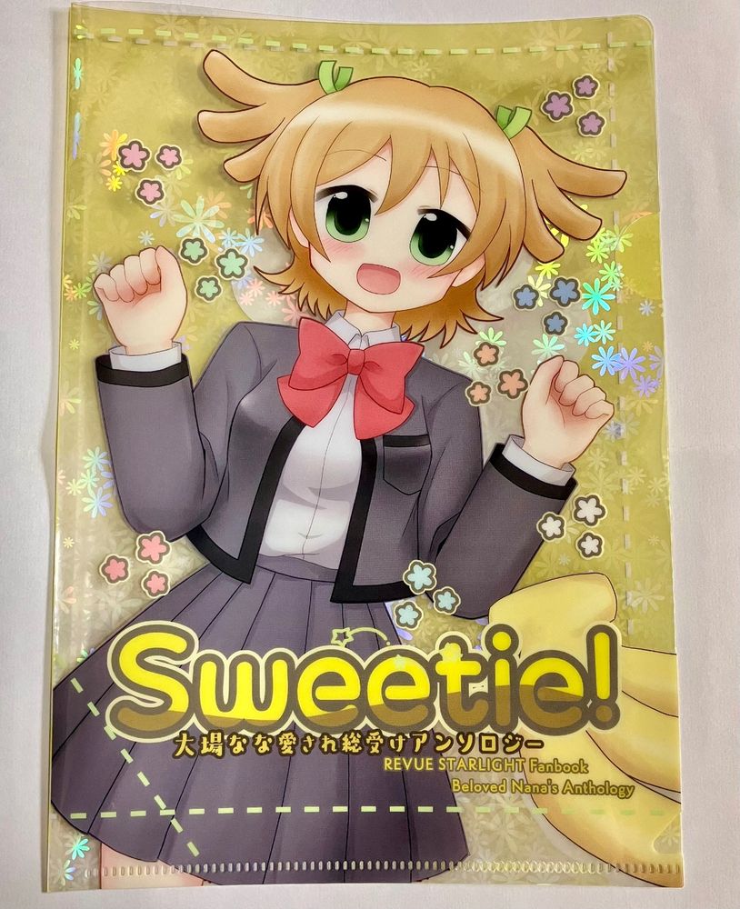 大場なな愛され総受けアンソロジーのノベルティその2。A5クリアファイルの実物写真。表紙デザインが印刷されていて、背景は透明になっていて、花柄のホログラムがキラキラしている。