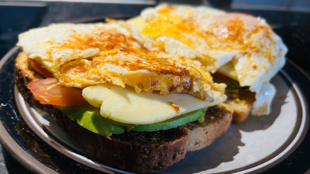 Two slices of bread with slices of (bottom to top) avocado, tomato and cheddar, betopped with fried eggs sprinkled with hot smoked paprika and Tabasco sauce (I’d use Frank’s sauce but have run out).