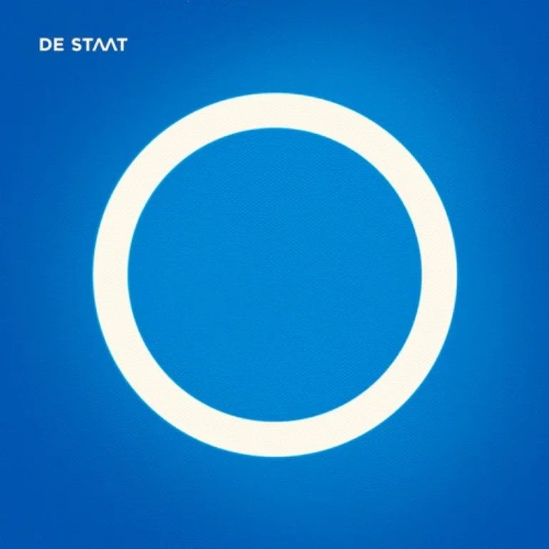 Cover art for De Staat's album "O". It depicts a simple white circle on a textured, bright blue background. The band's name/logo adorns the top-left corner. The band is vague as to whether the circle is just a circle, a letter, a number, an ouroboros, or any combination thereof, but the stark simplicity of the cover does bring this ambiguity to the forefront; effective minimalism for artistic ends.