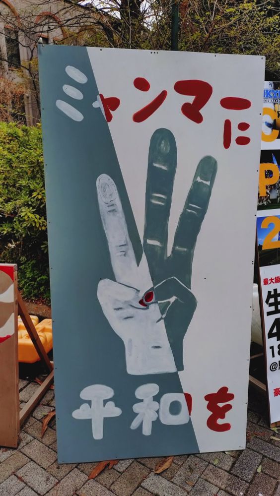 「ミャンマーに平和を」と書かれた立て看。中央に民主派のシンボルである三本指を開いた手が描かれている。