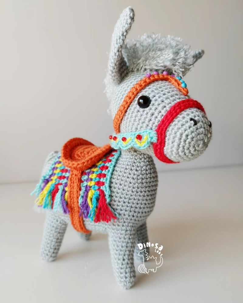 Amigurumi de un burrito gris con adornos muy alegres y llamativos