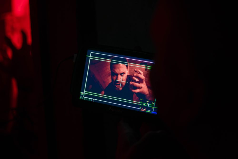 Man standing in a small abandoned space lit by red lights screaming into a camera