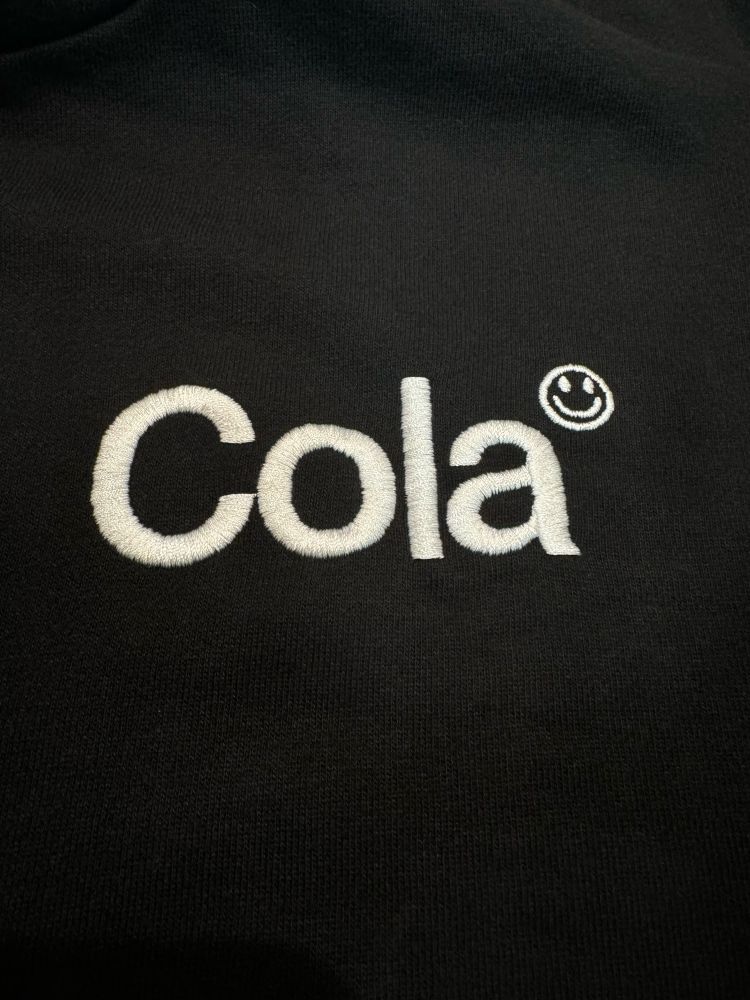 Embroidered Cola logo with superscript smiley face 