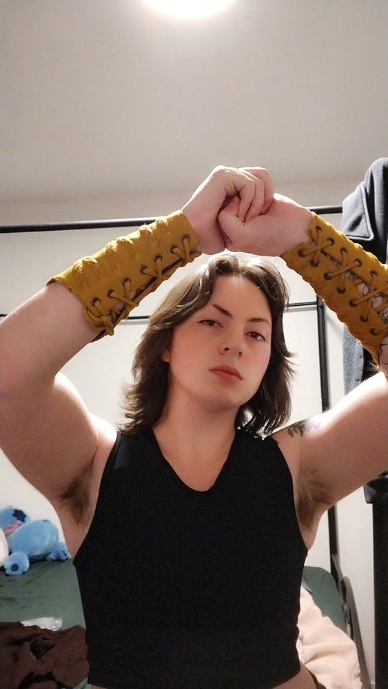 original poster posing with their arms up flexing their pecs in a costume: black binder, yellow arm covers