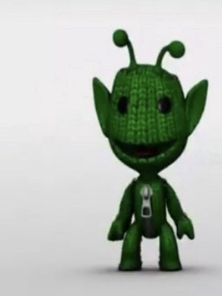 sackboy from the game littlebigplanet as an alien standing off to the right of the image
