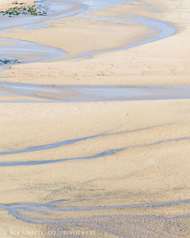 Wasser bildet Linien im Sand am Strand