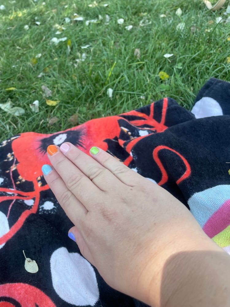 Mano derecha de mujer con cada uña pintada de un color pastel. De meñique a pulgar: verde, rosa, naranja, azul y lila.