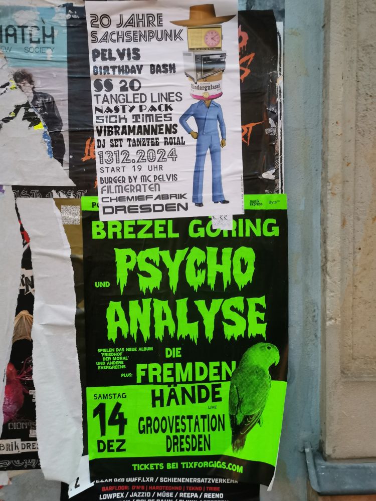 Zwei Plakate kleben übereinander.
Das obere zeigt ein Party von 20 Jahre Sachsenpunk am 1312 in der Chemo Dresden und das darunter eine von Brezel Göring plus Psychoanalyse plus die fremden Hände in der Groovestation Dresden 