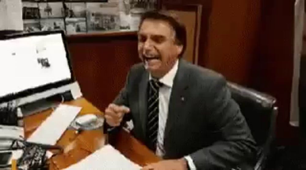 a man in a suit and tie is sitting at a desk laughing .