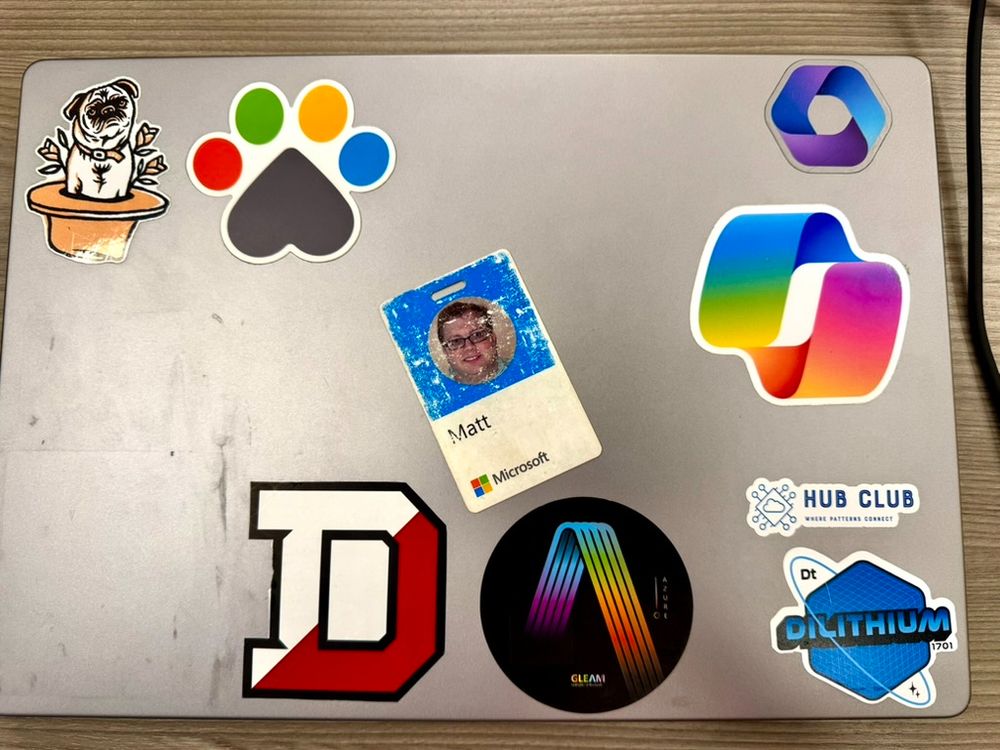 Laptop with a pug sticker, a dogs at Microsoft sticker, Denison sticker, Azure GLEAM, Dilithium, and Copilot stickers, and my Microsoft badge