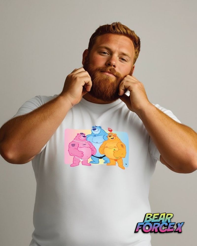 A bearded man with blonde hair poses playfully with both hands up to his face, wearing a white t-shirt featuring three colourful cartoon bears - pink, blue, and orange - arranged in a group. The “Bear Force X” logo appears in the bottom right corner