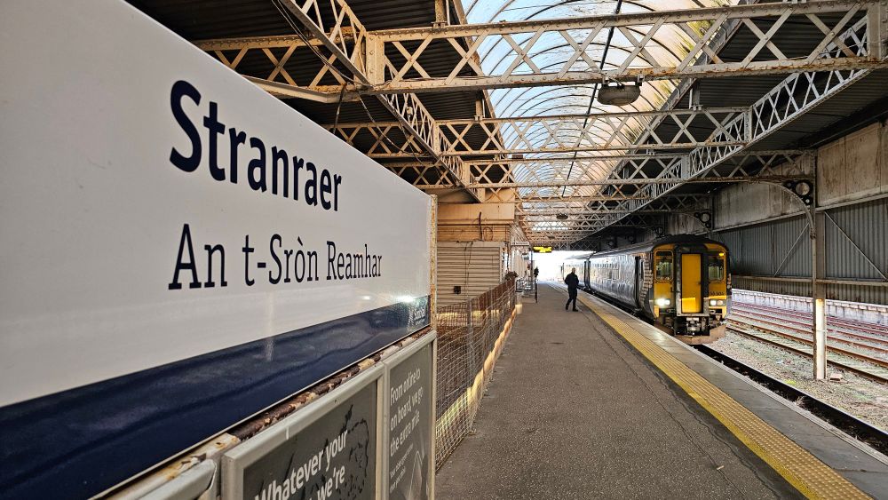 Stranraer station sign with a Class 156 waiting to depart