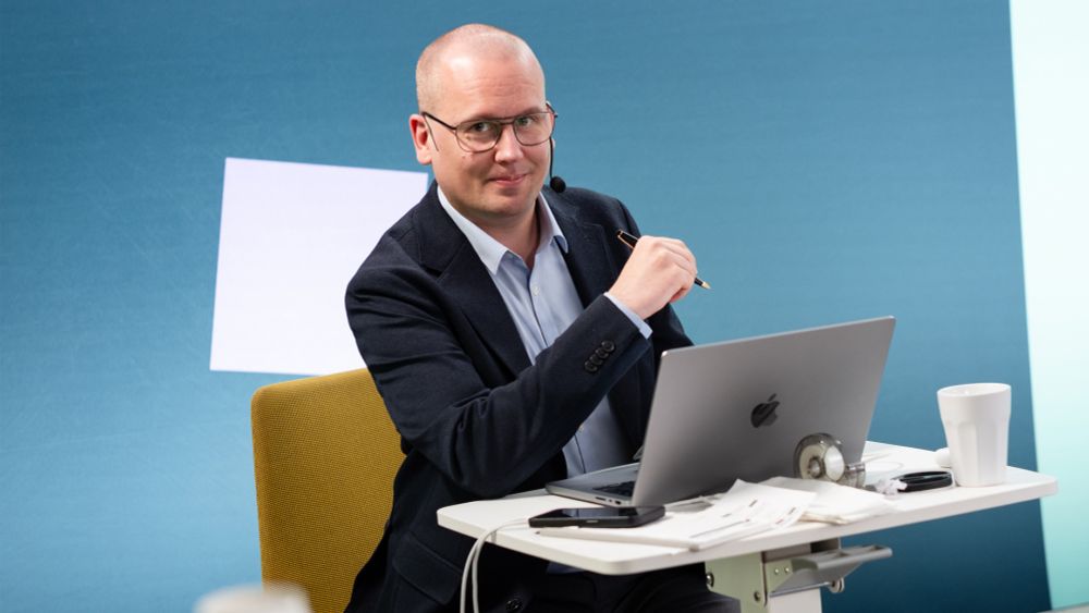 Karl Emil Nikka sitter vid en dator, omringad av kaffekopp, anteckningslappar och tejp. 