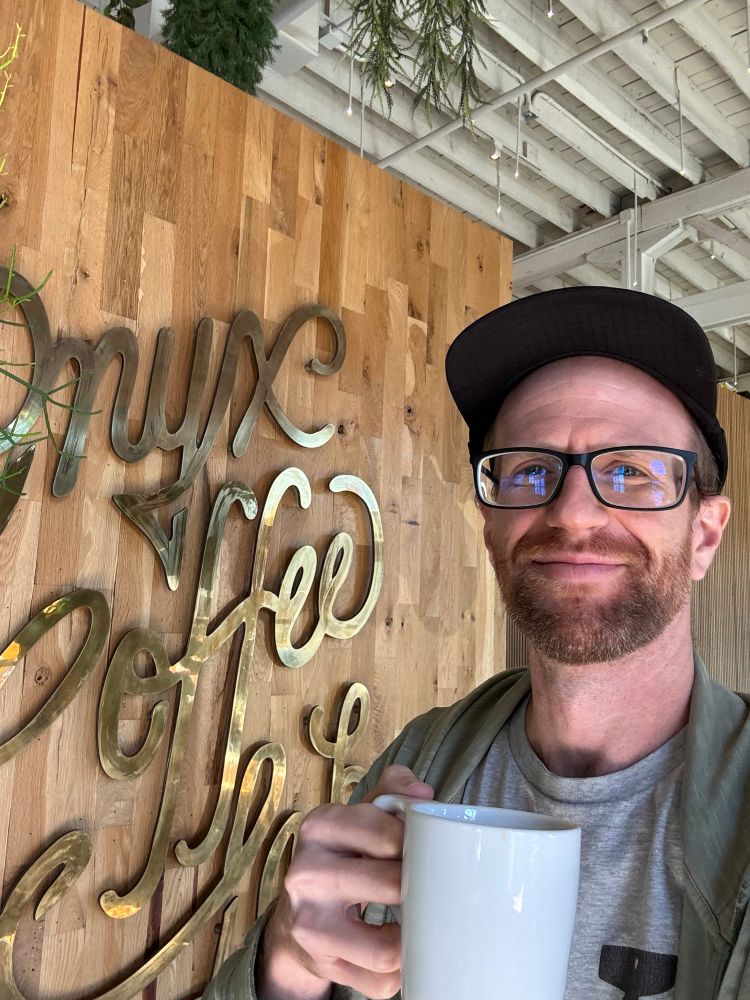 Man smiling with a mug of coffee in front of an Onyx Coffee Lab sign.