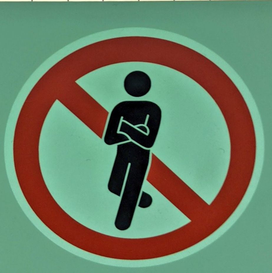Red circle with slash over a leaning stick figure with crossed arms.