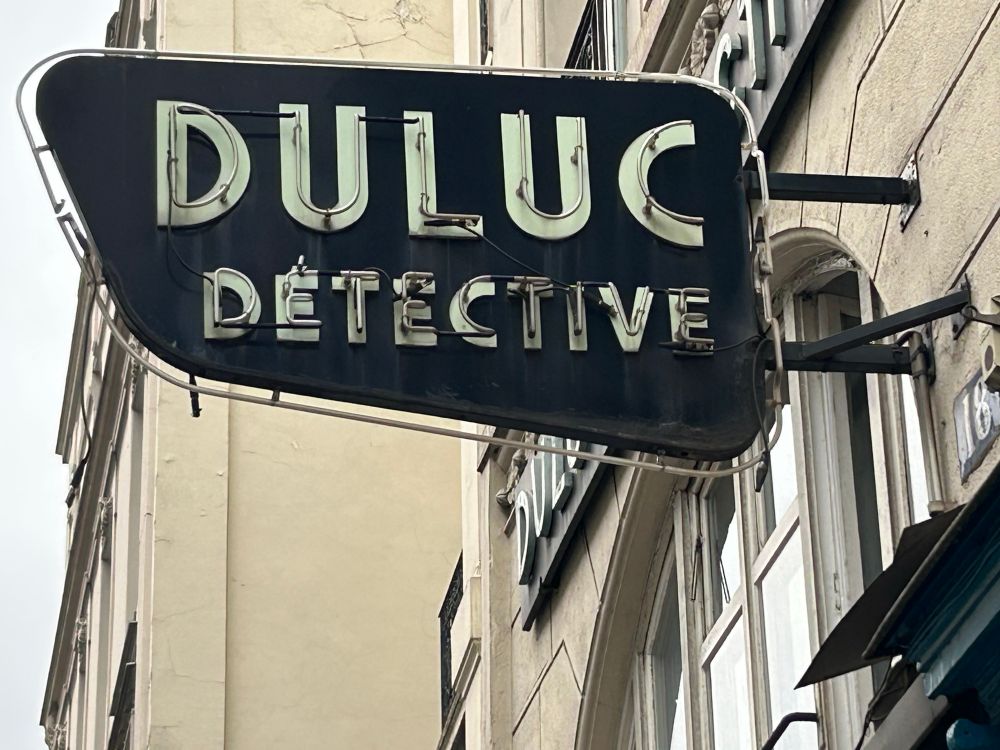 Neon sign on a facade: DULUC DÉTECTIVE.