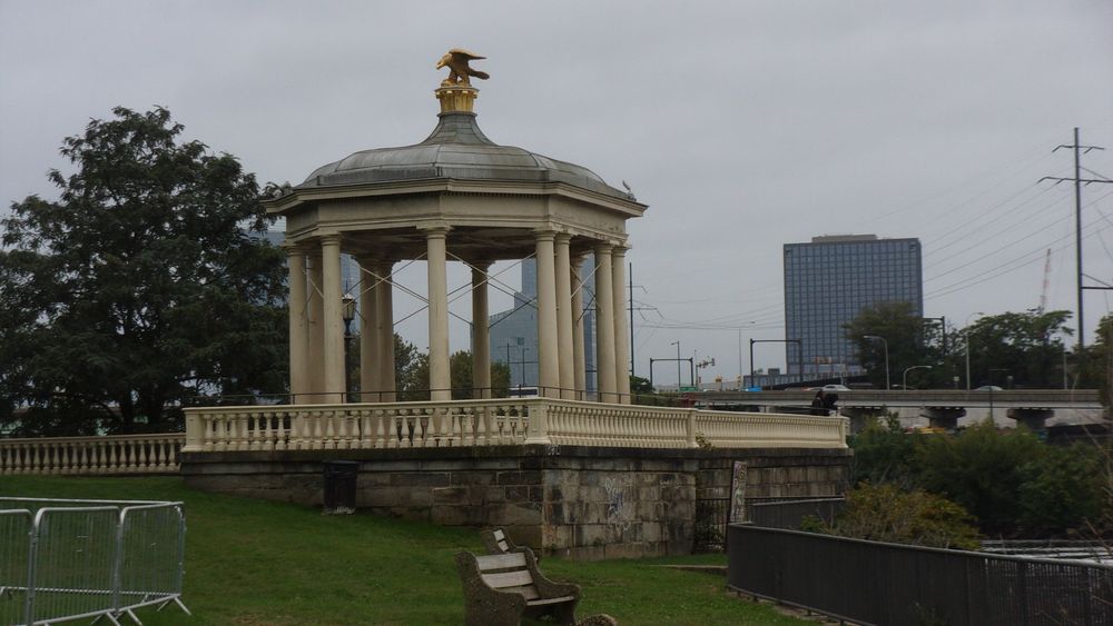 Art museum gazebo. Gazebo in center of frame with grassy field in foreground and a tree and building in the background.