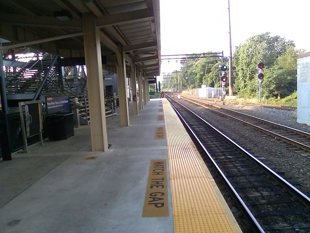 Fern Rock Transportation Center regional rail station looking northbound with tracks to the right and weather cover to the left. A yellow strip and the words watch the gap straight ahead.