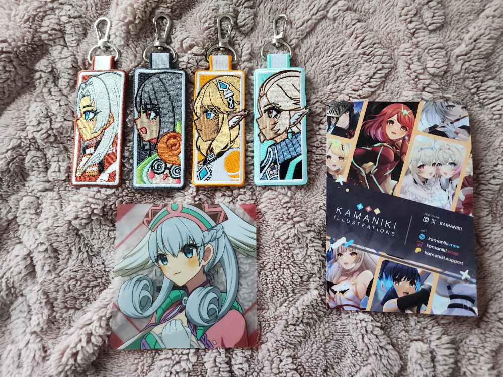 Four jet tags and a gacha card from the Kamaniki illustrations shop. At the top are the four jet tags featuring (from left to right) Elma, Lin and Tatsu, Celica, and Nielnail from Xenoblade Chronicles X/Definitive Edition. Below the jet tags is the gacha card featuring Melia from Xenoblade Chronicles/Definitive Edition. To the right of the jet tags and gacha card is a card promoting the Kamaniki Illustrations shop and which social media platforms you can follow it on. 