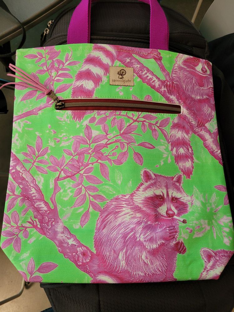 A handmade totebag featuring a lime green and purple print of raccoons smoking cigarettes. 