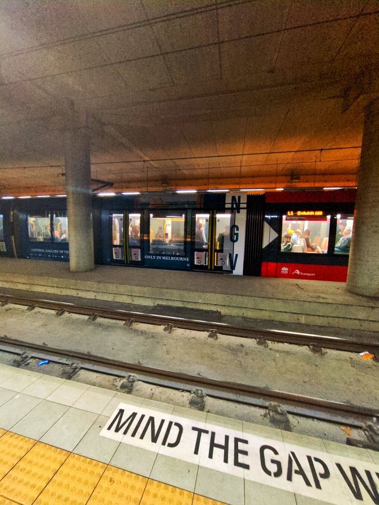 A red Sydney tram covered in a navy blue wraparound ad that reads 