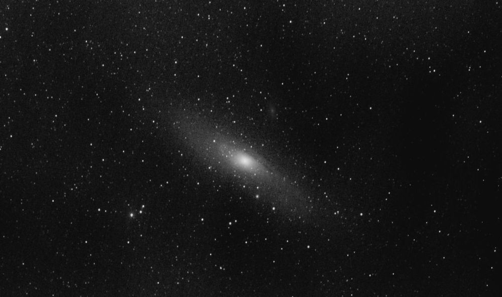 The Andromeda Galaxy at centre shown in mono. Galaxy M110 above. Many star dots. 