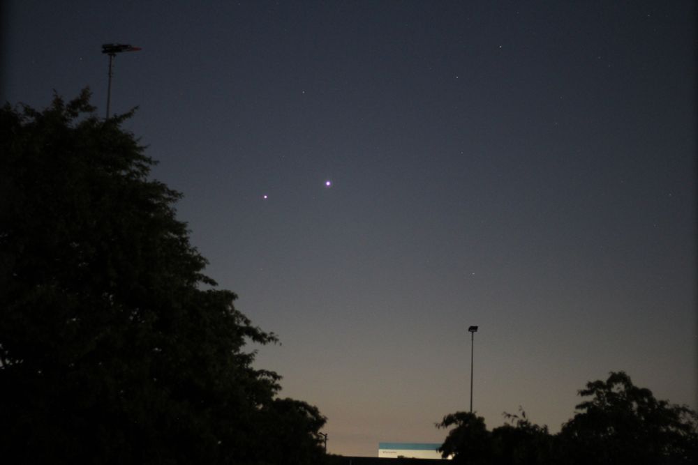 Planets Venus and Jupiter dots at left of centre. Trees and floodlights in foreground. 