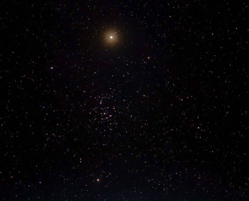Planet Mars a bright star-like object above centre. Star cluster the beehive at centre with numerous other star dots. All on a dark background. 