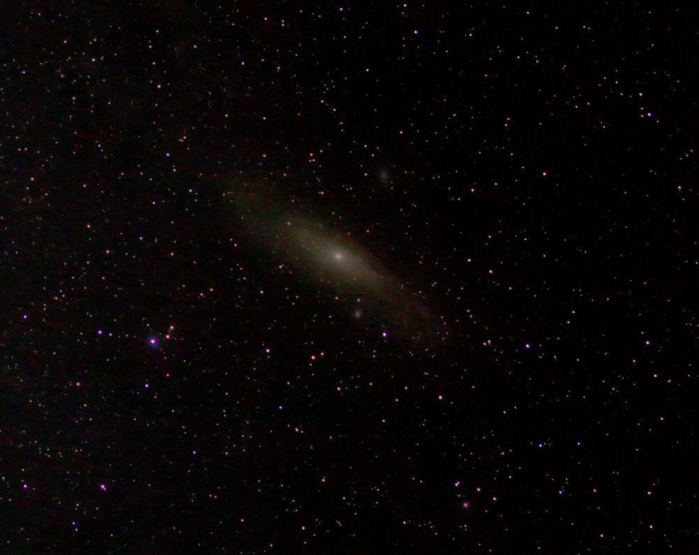 The Andromeda galaxy at centre. Fainter galaxies above and below. Many star dots. 