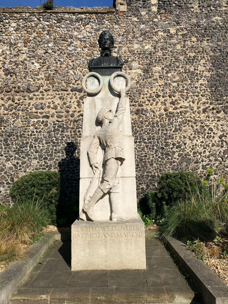 A memorial to Edith Cavell, British nurse executed by the Germans for spying during WW1. Pale stone monument showing a young man in WW1 military uniform lifting wreaths up to a bronze bust of Edith Cavell