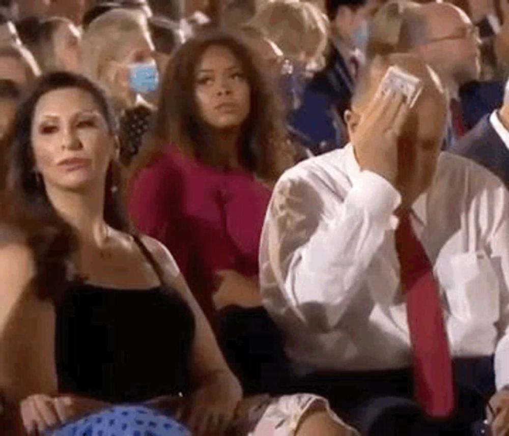 a man is covering his face with a dollar bill while sitting in a crowd of people at a concert .