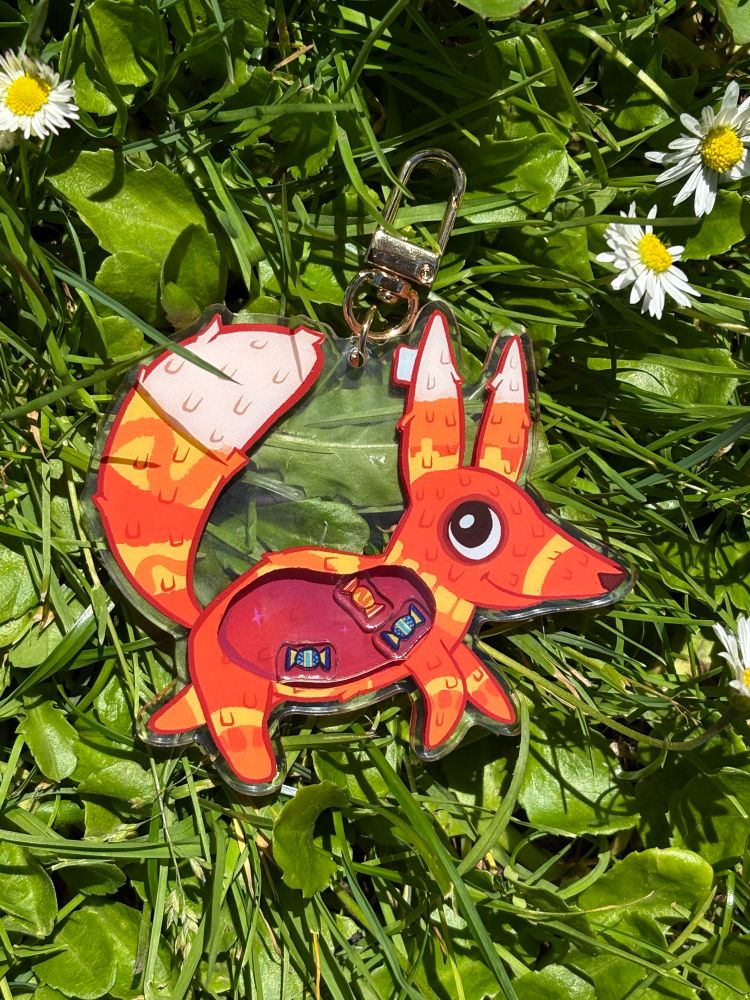 Pretztail shaker charm with three candies inside an orange belly. 