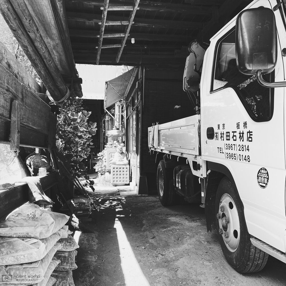 High-contrast monochrome photograph of a scene at "Murata Stone Works", a small company making stone sculptures and other stone products in the Hasunuma-cho neighborhood of Itabashi Ward in Tokyo, Japan.